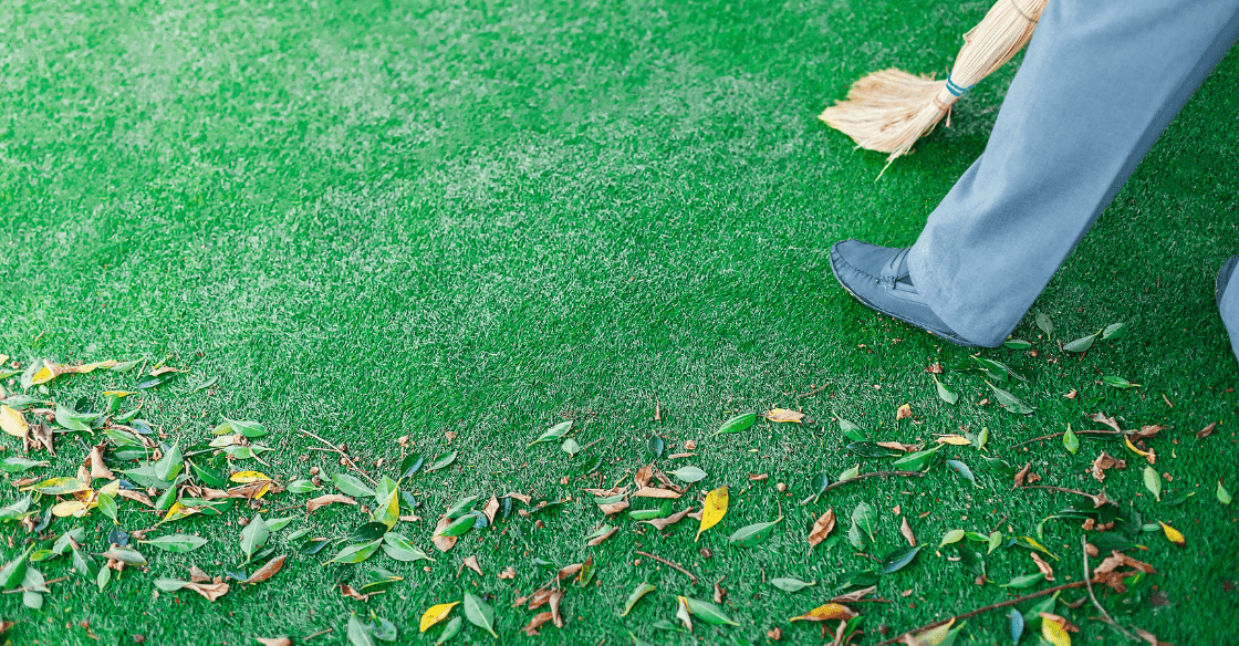 A man sweeping leaves off his artificial lawn, demonstrating how easy the lawn is to maintain. 